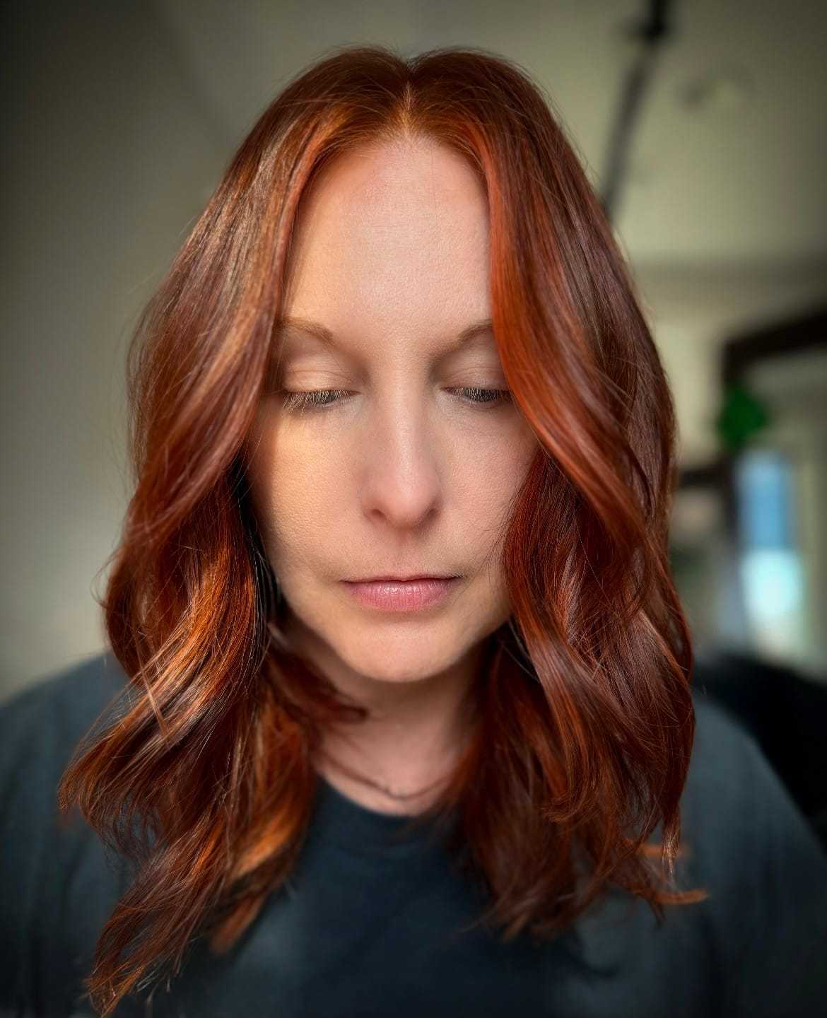 Woman with red hair looking down in a softly lit room.