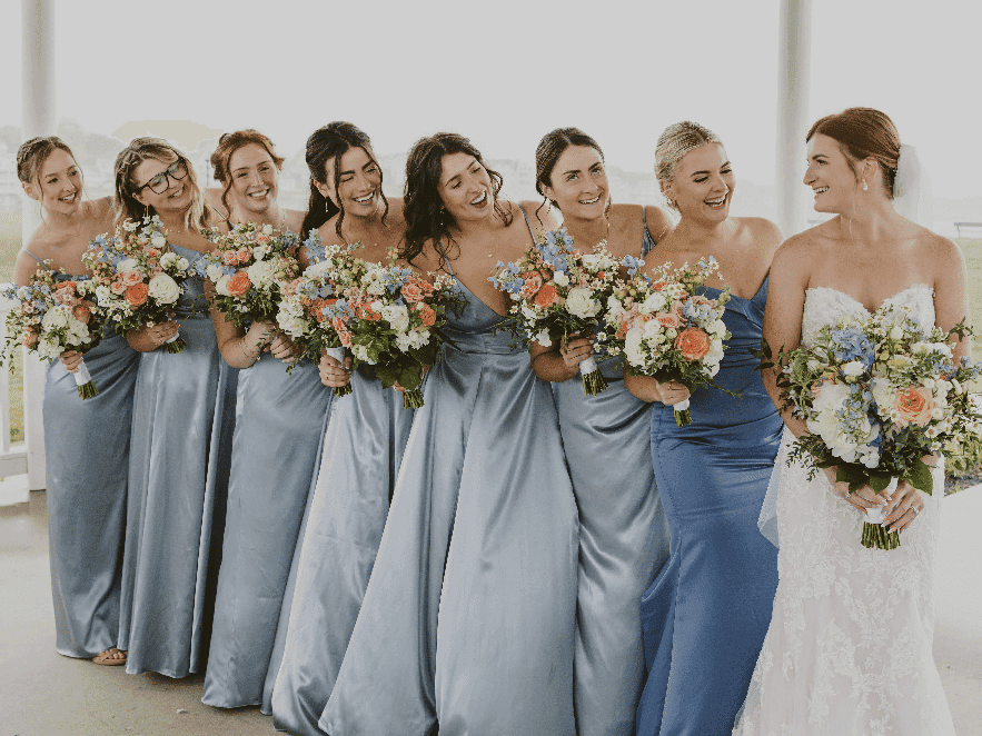 Bride and bridesmaids in blue dresses holding bouquets, standing in a gazebo.