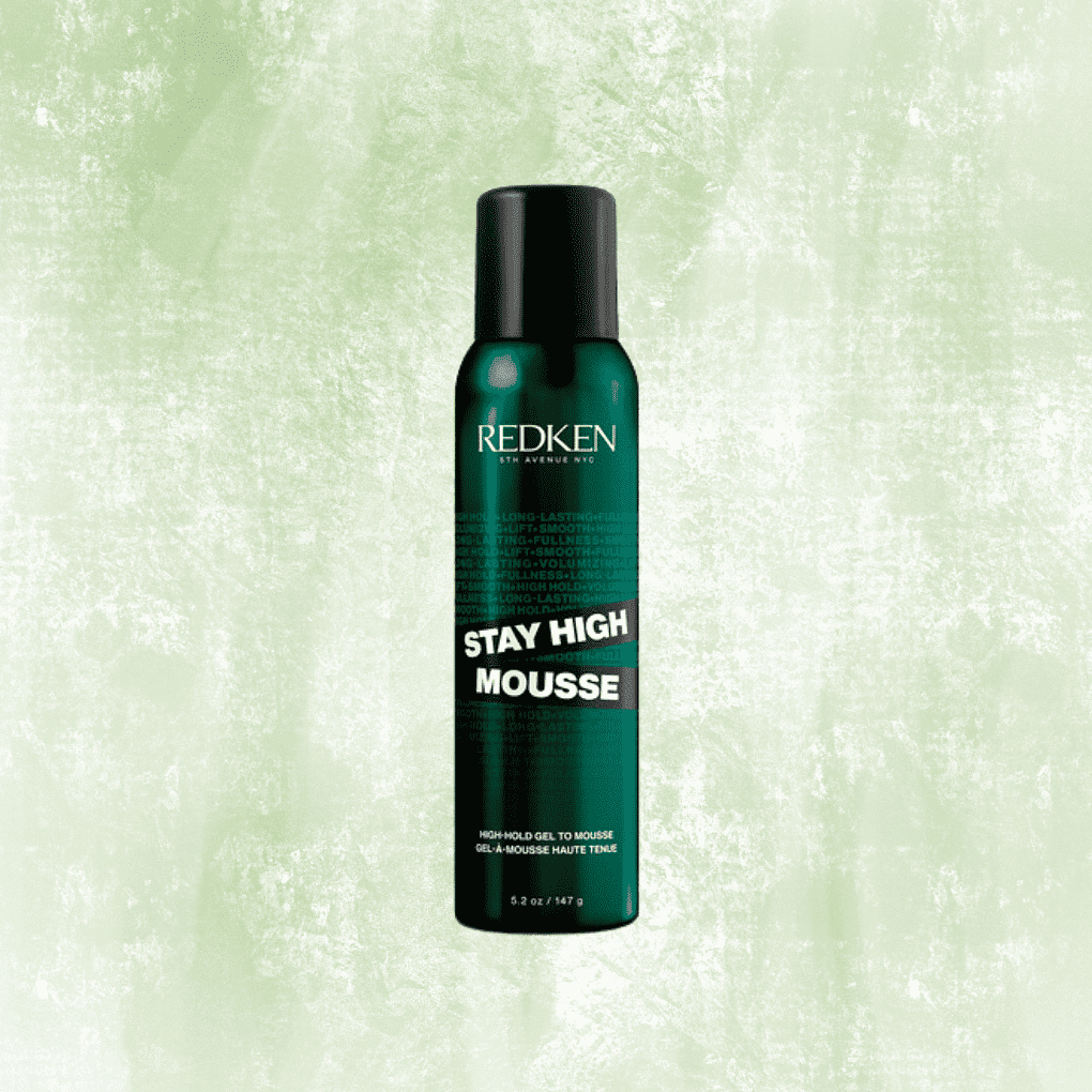 Redken Stay High Mousse bottle against a textured green background.
